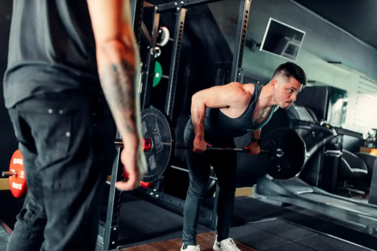 Client in a bent over barbell row with a BTX coach in the foreground
